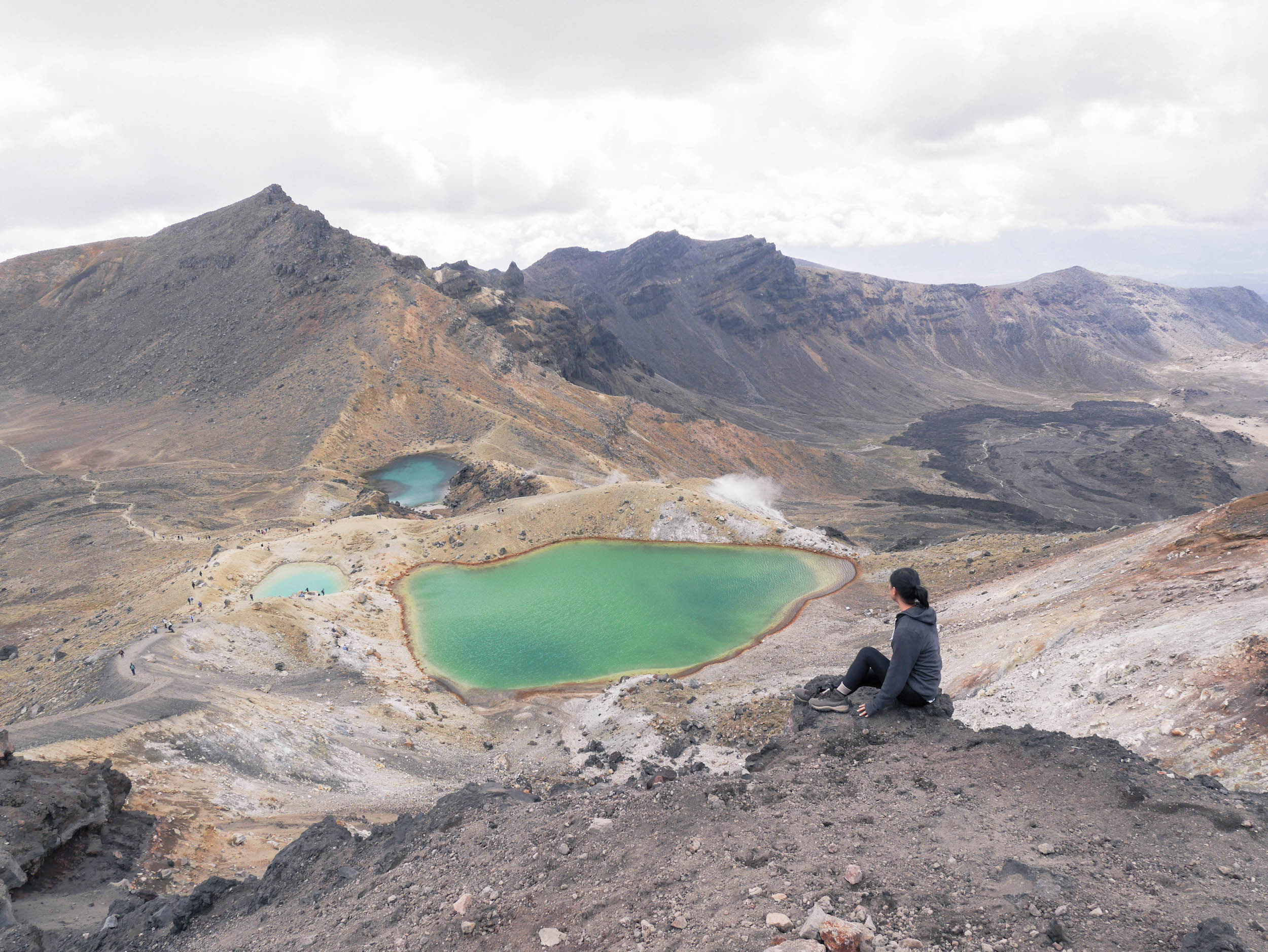 A girl sitting on top of a viewpoint looking at two sulfuric lakes